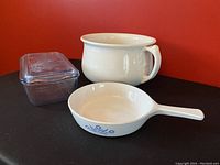 Photo showing Corning Ware blue cornflower pattern frying pan with handle, Fire King white casserole with lid, and heavy ironstone chamber pot.