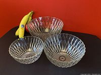 Three clear glass vintage nesting bowls on black surface with red background and bananas for scale. Shows size difference and textured diamond pattern on bowls.