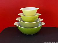Stacked view of four nested vintage Pyrex Verde Cinderella mixing bowls in varying green shades with white interiors.