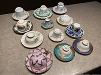 All 12 vintage teacups and saucers shown upside down to display marks and patterns on saucers and cup bases.