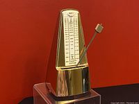 Front side view of the golden triangular metronome showing the tempo scale and pendulum arm.