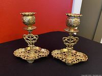 Pair of vintage brass ornate candlesticks shown on black surface with red background