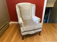 View of the chair from a front angle showing the high back and winged sides with fabric upholstery and walnut legs.