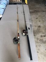 Two fishing rods laid flat on a table, one with wooden handle and reel, other with black foam handle and reel