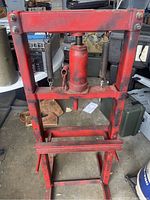 Front view of red barrel jack shop press showing steel frame, center jack without handle, and coil springs on each side.
