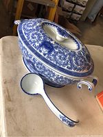 Side view of the Bombay soup tureen with lid and ladle on a table, showing the intricate blue floral pattern.
