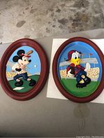 Two Disney ceramic plaques side by side, showing Mickey Mouse playing baseball and Donald Duck playing football, both oval shaped with reddish-brown frames.