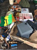 Overview photo of assorted vintage items on table including electronic casings, crocheted textiles, red and white striped small boxes, framed art, and miscellaneous parts.