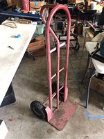 Full view of two wheel dolly leaning against a table, showing entire frame, handle, and base plate
