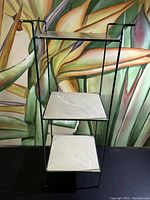 Front view of 3 tier shelf stand showing metal frame and three light-colored marbled tile shelves