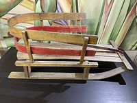 Side view of the antique sled showing wooden construction with red metal runners and support handles.