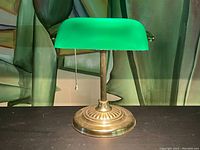 Front view of vintage banker’s desk lamp showing curved green glass shade and brass base with pull chain.
