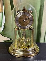 Full view of the Birks clock with brass base, clock face, rotating pendulum balls, and clear glass dome covering.