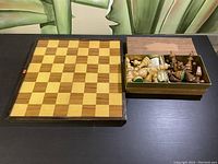 Chessboard and box containing chess pieces displayed side by side on a black table surface.