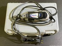 Dremel Multi-Pro Model 395 rotary tool placed on top of the original light grey plastic carrying case, showing the tool, attached power cord, and two-prong plug.