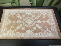 Full view of the tan and off-white vintage entryway rug showing floral and geometric pattern.