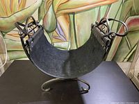 Side angle showing curved leather liner and metal frame with decorative scroll elements and ball finials.