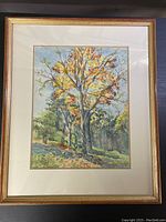 Full view of framed watercolour painting showing a tree with autumn leaves in a natural setting, in gold-tone frame with cream matting.