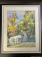 Framed watercolour artwork showing a white rural house with autumn trees, mounted on cream mat within a gold frame.