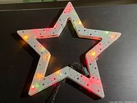 Front view of white star-shaped Christmas ornament illuminated with multicolored LED lights, showing star-shaped perforations on the frame.