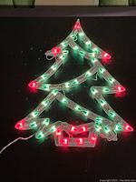 Front view of illuminated Christmas tree with red and green bulbs lit on black surface showing detail of shape and lights