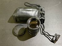 Overview of the lens with front and rear caps and accompanying black drawstring pouch on a dark surface.