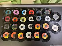 Top down view of 13 assorted 45 RPM records showing various colored labels and usage wear.