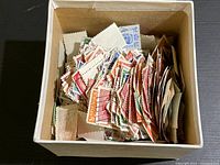 Box filled with numerous assorted vintage stamps showing varied colors and sizes.