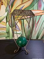 Full view of vintage metal plant stand with lattice top and curved legs in front of a colorful mural background.