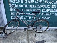 Full side view of the gray Miyata Terra Runner bicycle leaning against shipping container background showing frame, tires, pedals, saddle, and handlebar.