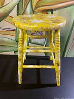 Front view of a yellow vintage wooden stool showing worn paint and turned legs.