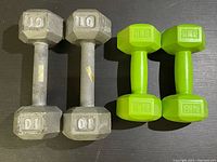 Top-down view of one pair of gray 10lb cast iron dumbbells and one pair of bright green 2lb plastic-coated dumbbells side by side on a black surface.