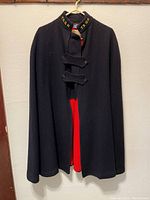 Front view of the black nurse's tunic showing the red lining inside and front toggle closures.