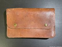 Front view of brown leather WW2 Canadian Engineer's tool bag with two brass snap buttons and embossed Canadian broad-arrow marking with 1943 date and manufacturer.