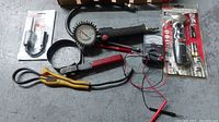Photo of assorted automotive tools including gauge, pliers and electrical tester on concrete floor.