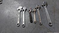 Photo of six assorted crescent wrenches of varying sizes laid out on a concrete or metal surface.