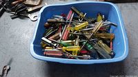 Blue plastic container filled with assorted old screwdrivers and some small hand tools on a concrete floor