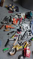 Top view photo of assorted hand tools laid on concrete floor showing a variety of screwdrivers, clamps, hand saws, and measuring equipment.