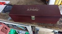 Closed view of dark wood box with KPMG logo on top, showcasing the branded casing for the wine accessory set.
