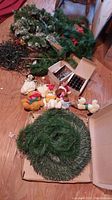Image displaying two different artificial wreaths, several stuffed animals, and boxes of Christmas string lights all on a wooden floor.