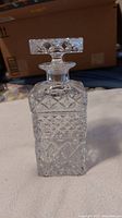 Front view of square crystal decanter with stopper, showing diamond cut and hobnail pattern.
