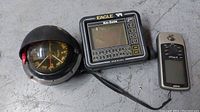 Photo showing the Eagle Nav-Guide GPS unit, a marine compass in black dome casing, and the Garmin GPSmap 76 handheld GPS unit.