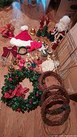 Full assortment of Christmas decorations including Santa hat, bells, ribbons, greenery wreath, wicker wreaths, ornaments, and decorative berries arranged on floor.