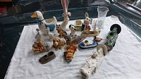 Various ceramic animal and character figurines arranged on white cloth on glass table