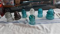View of seven vintage glass hydro insulators in various colors and sizes laid out on cloth.