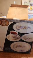 Closed box of Royal Oak Violet's 20-piece dinner set showing floral patterned plates and cup on the front.