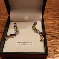 Pair of sterling silver earrings displayed inside a black jewelry box with a white interior, showing five rectangular cut gemstones in different colors each.