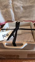 Gift set comprising a white ceramic baking dish and black and white striped dish towel tied with a black ribbon, showing the Oui brand tag.