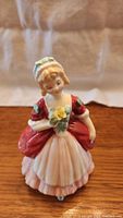 Front view of the Royal Doulton Valerie figurine showing the figure holding a yellow rose in a red dress and white apron.