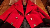 Front view of red wool coat with black trim, showing double-breasted buttons and lapels laid out on a table.